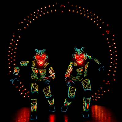 Two performers in illuminated suits pose dramatically against a dark background with circular red LED lights.
