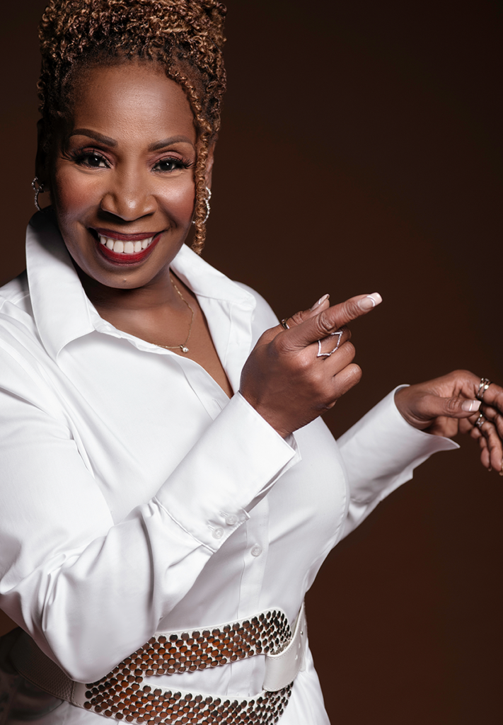 Person wearing a white shirt smiles and points to the side, posing against a dark background.