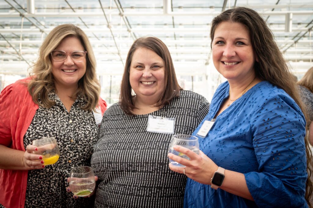 Three women smile while holding drinks