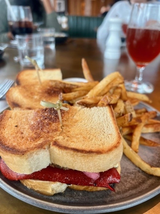 A plate with a toasted sandwich served with French fries; a drink in a glass is in the background.