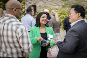 A woman in a green blazer smiles and interacts with two men during a PNC pop up event. Other attendees are seen mingling in the background.