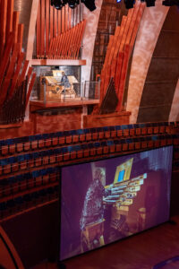 Kraybill plays a large pipe organ on stage, their performance projected onto a screen in an auditorium during Alzheimer’s Awareness Month.