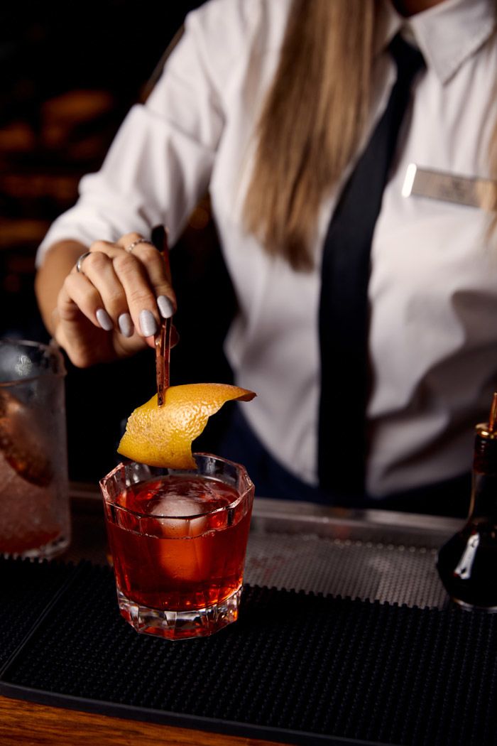 A bartender in a white shirt and black tie garnishes a cocktail with an orange peel at the Horsefeather Social bar.