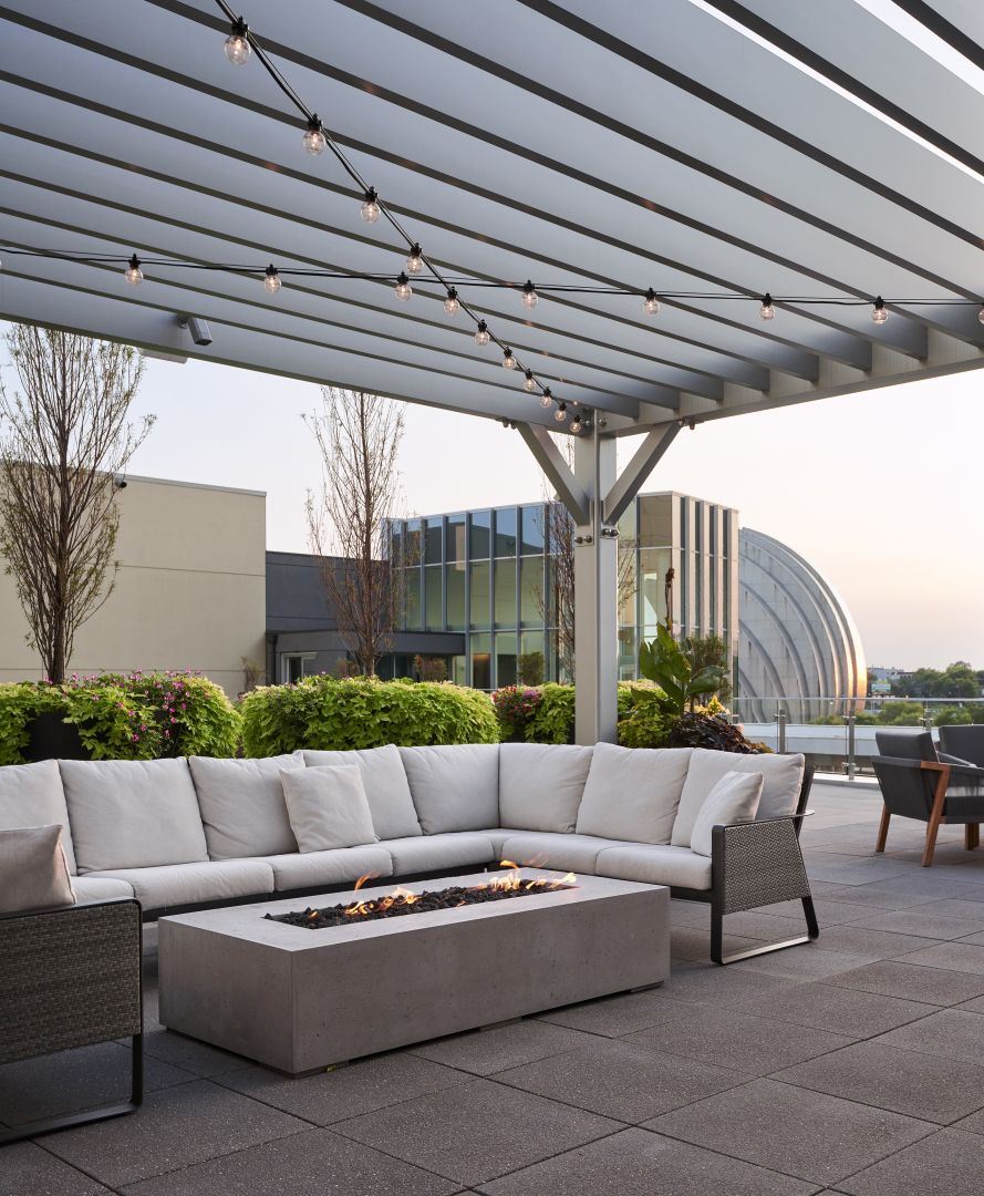 The modern outdoor terrace of Loews Kansas City Hotel with cushioned seating, a fire feature, and a view of city buildings, including the Kauffman Center's north shells. 